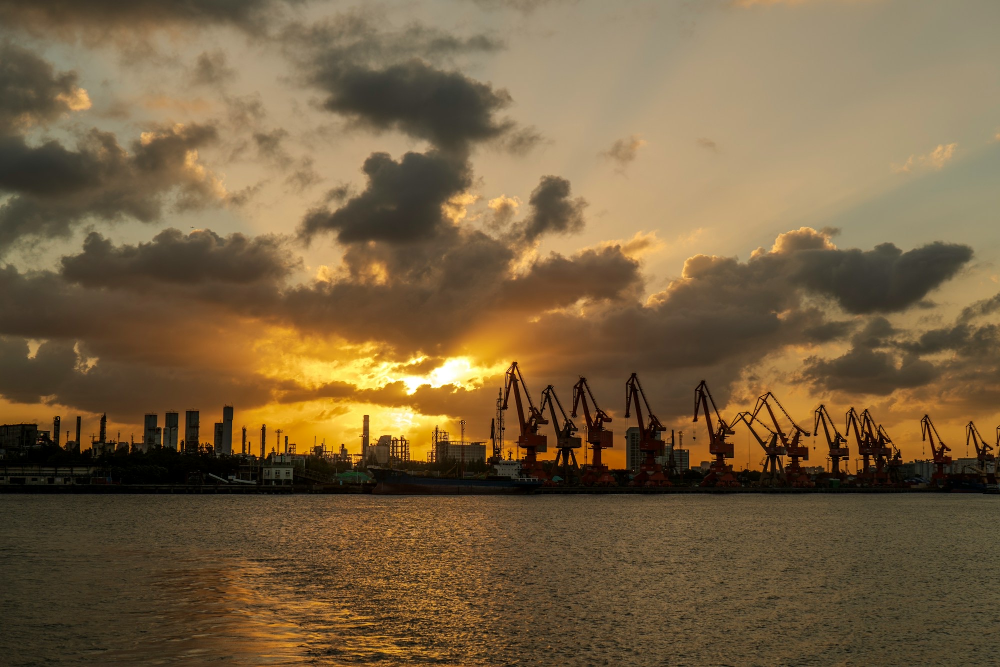 Silhouetted port cranes and city skyline at sunset, seen across the water